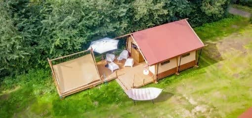 Foto aerea del Cozy Lodge con il tetto rosso e la veranda, il Teeny Lodge accanto e un'amaca sul prato