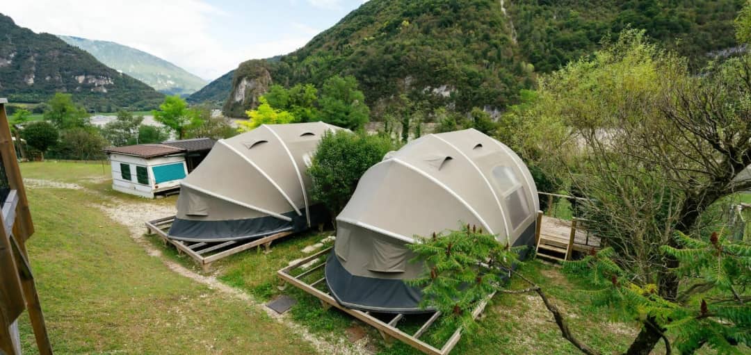 Due Big Oak Lodges XS con telo a cupola su piattaforme di legno, tra verdi montagne con pareti rocciose