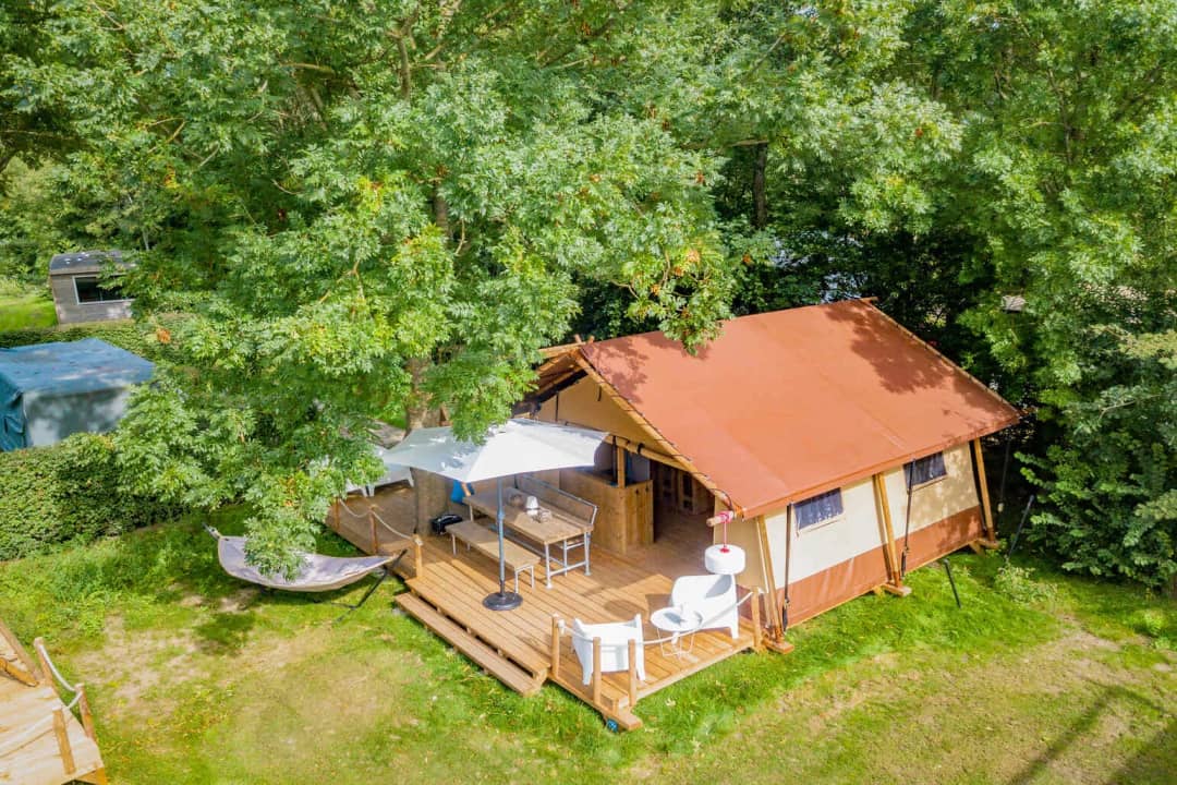 Foto aerea del Cozy Lodge con il tetto rosso-marrone sotto alberi ad alto fusto, con ombrellone, tavolo da pranzo e amaca vicino alla veranda