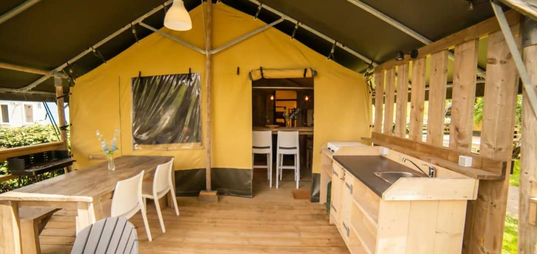 Veranda coperta del Safari Lodge con tavolo da pranzo in legno, sedie bianche, cucina all’aperto con lavello e barbecue