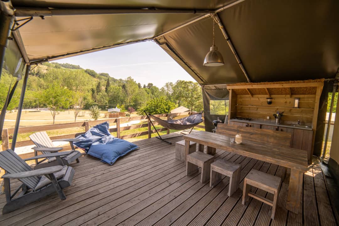 Veranda del Safari Lodge per 2-6 persone con sedie da giardino, pouf blu, amaca e un lungo tavolo con sgabelli affacciato su un prato