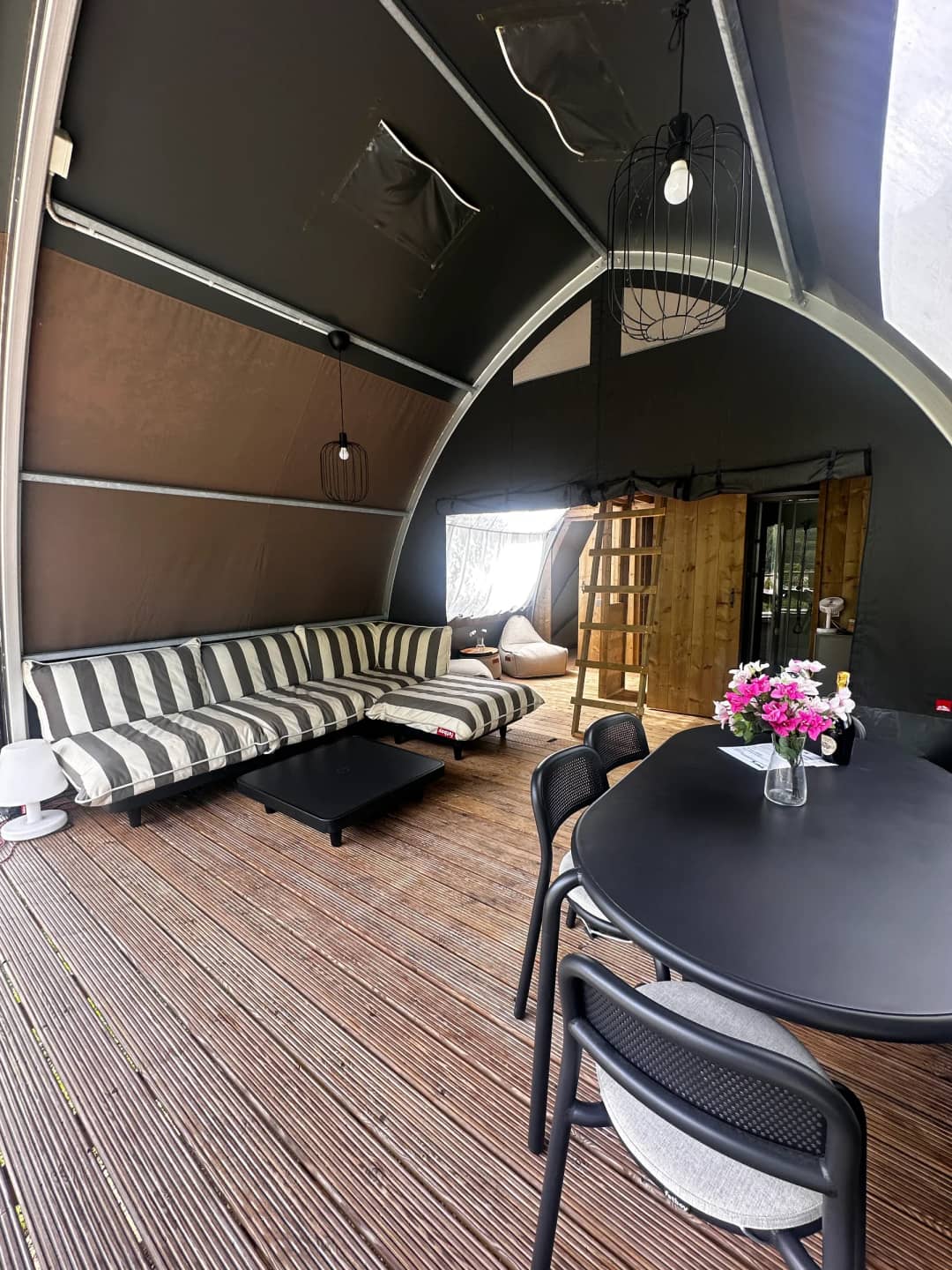 Zona giorno del Big Oak Lodge XL con divano a strisce, tavolo da pranzo nero con fiori e una scala di legno