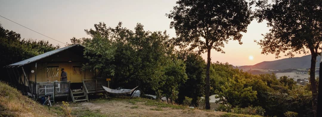 Piscina del Camping Casa Tartufo con bagnanti, lettini rossi e vista sulle verdi colline delle Marche